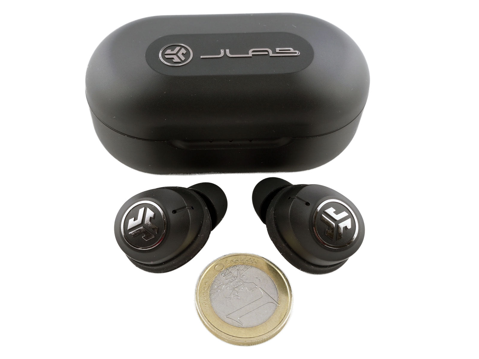 JLab JBuds Air ANC True Wireless Earbuds In-Ear Kopfhörer Ein geschlossenes Ladeetui mit einem silbernen Jlab Logo und Schriftzug auf der Oberseite, zwei kabellose Earbuds mit silbernen Logo auf der Voderseite und eine 1-EUR-Münze für den Größenvergleich auf weißem Hintergrund.