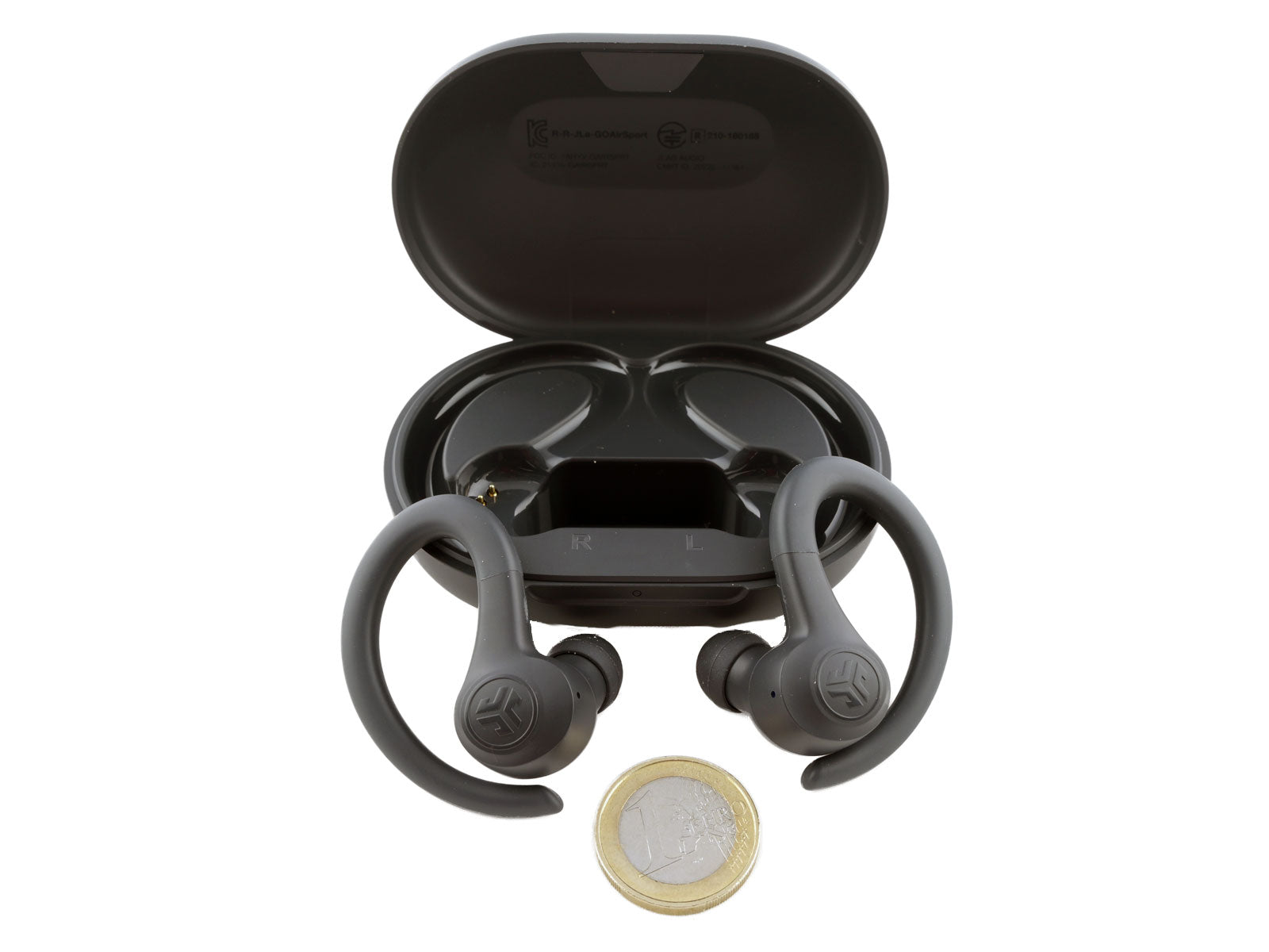 JLab GO Air Sport True Wireless Earbuds In-Ear Kopfhörer Schwarze kabellose Ohrhörer befinden sich vor einem offenen Ladeetui, das zum Größenvergleich über einer einzelnen Euro-Münze positioniert ist. Die Ohrhörer verfügen über Ohrbügel für sicheren Halt.